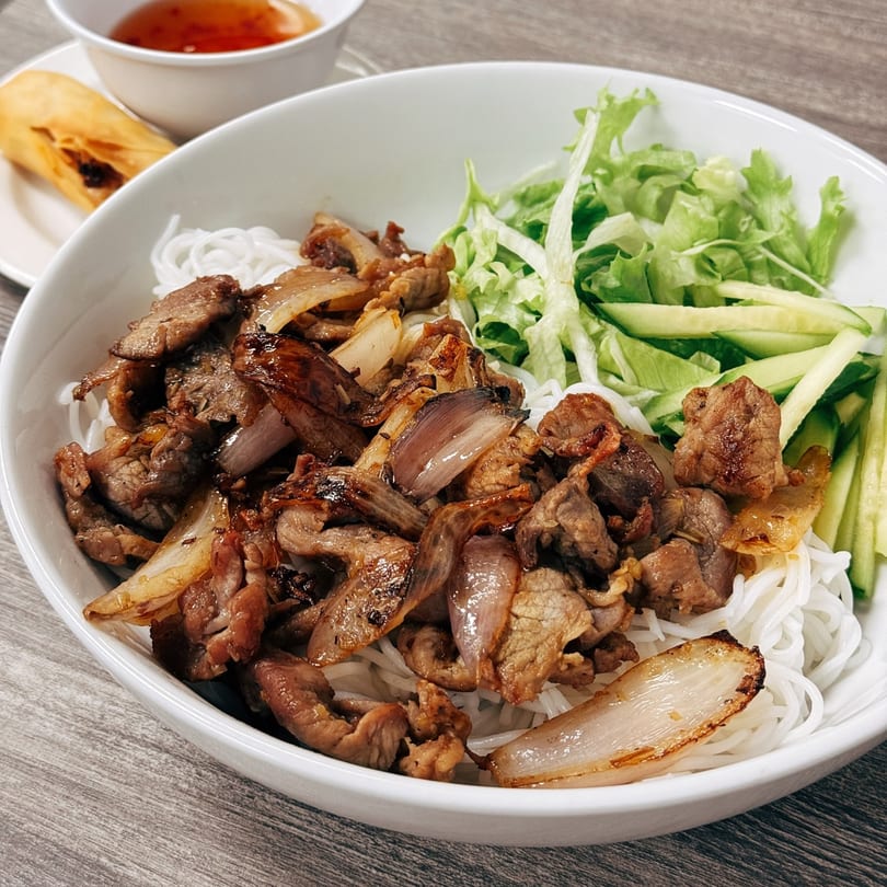 Vietnamese vermicelli bowl with grilled pork, onions, lettuce, cucumbers, and a spring roll.