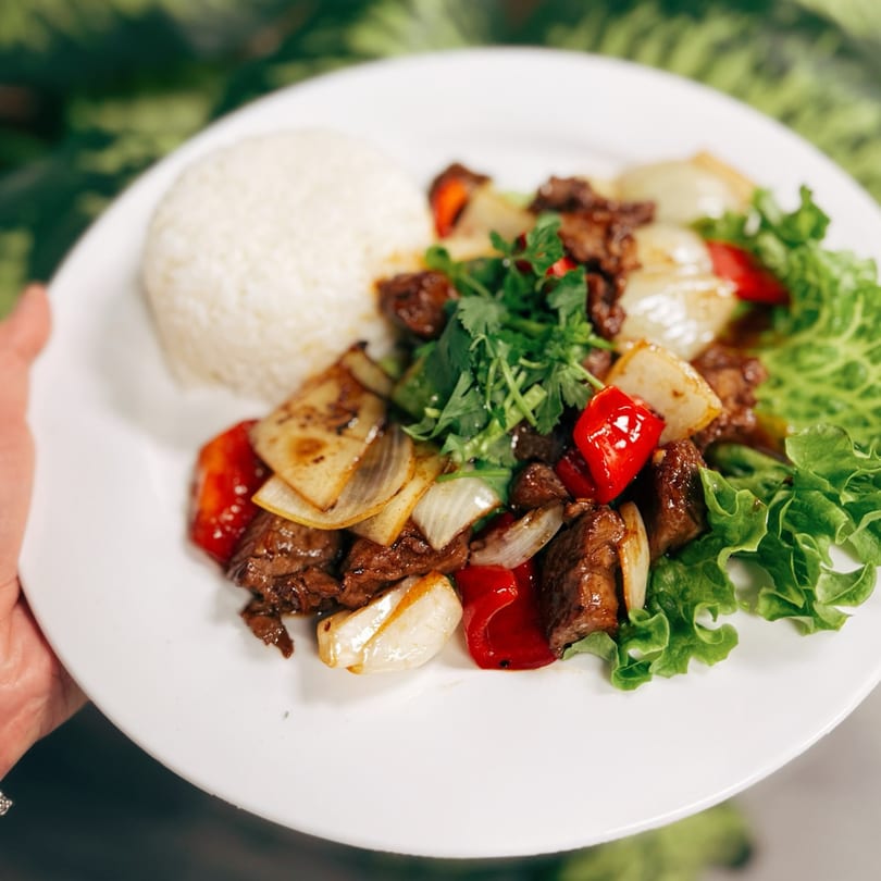 A plate of Vietnamese shaking beef (Bo Luc Lac) with rice, onions, bell peppers, and lettuce.