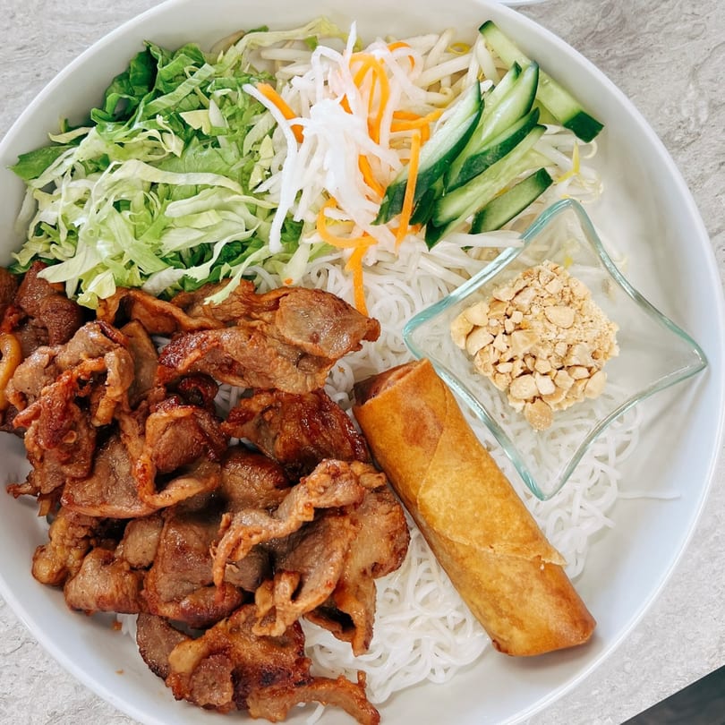 A Vietnamese vermicelli bowl with grilled pork, lettuce, pickled vegetables, a spring roll, and peanuts.