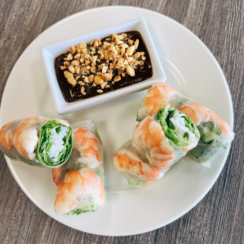 Four fresh Vietnamese shrimp spring rolls with a side of peanut dipping sauce on a white plate.