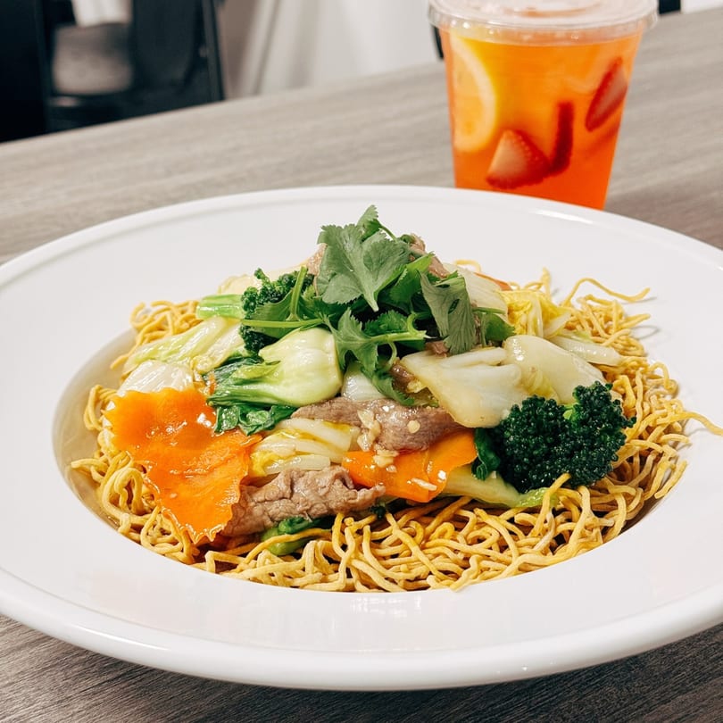 Crispy Vietnamese egg noodles with beef, broccoli, bok choy, carrots, and cilantro, with a drink.